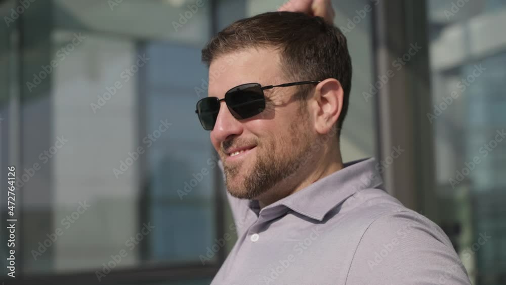 Slow motion side view of happy businessman wearing sunglasses and holding coffee walking out of the office Stretch take a break enjoy the sunshine On a sunny afternoon Slow motion side view of happy businessman wearing sunglasses and holding coffee walking out of the office Stretch take a break enjoy the sunshine On a sunny afternoon