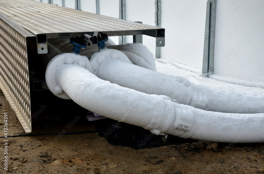 cooling register of pipes under the ice surface. rows of frozen tubes. strong pipes, hoses are twisted on the lawn in the park. A portable cooling device stands nearby and cools the coolant mixture