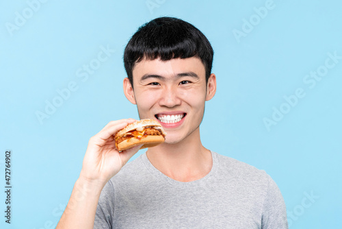 Young Asian man smiling and holding Hamburger about to eat in isolated light blue color studio background