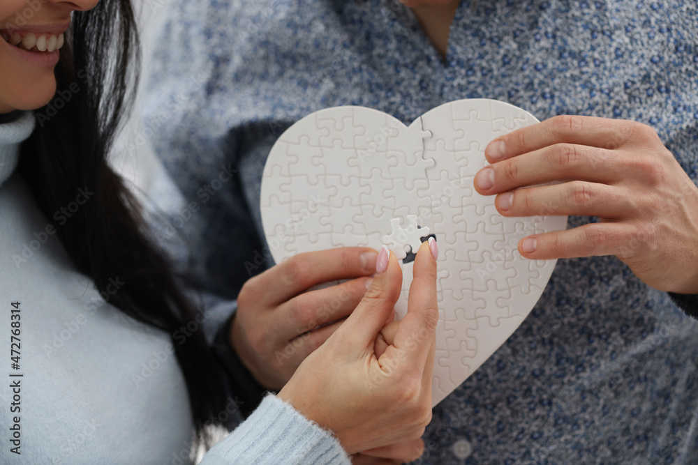 Woman and man fill empty space with missing piece of white heart puzzle
