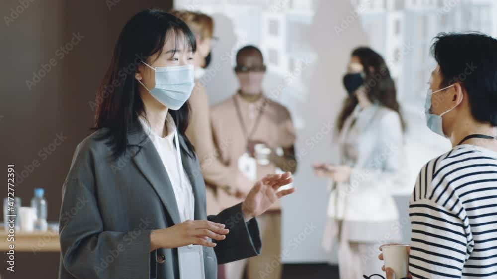 Two Asian female colleagues in protective face masks talking on business event in times of covid-19 pandemic Two Asian female colleagues in protective face masks talking on business event in times of covid-19 pandemic