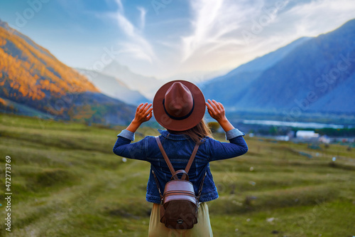 Back view of hipster girl wanderer wearing hat and backpack traveling alone on mountain valley in Georgia country photo