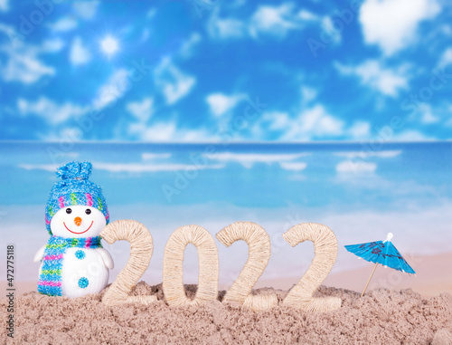 Snowman in the sand of the beach and the inscription 2022 under umbrella