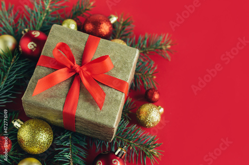 Gift box with spruce branches, red and golden balls on a red background. Holiday concept.