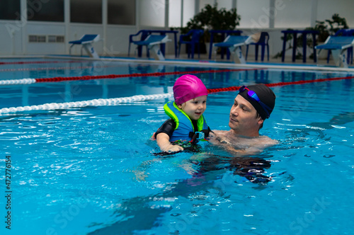 Happy father enjoying teaching his young daughter how to swim in swimming pool. Swimming lesson in the indoor pool, Swimming family.