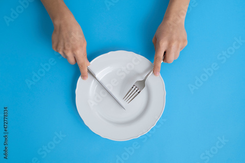 Woman hands holding cutlery on empty plate on blue background.