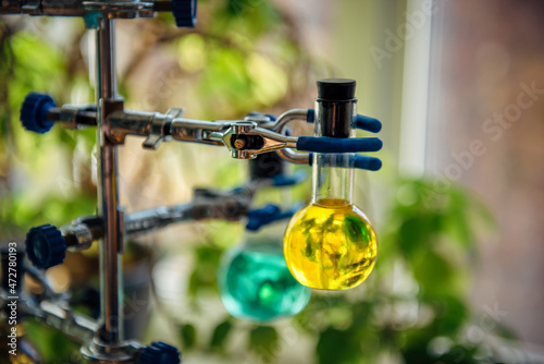 Tripod with round glass flasks and colored liquids on blurry background in chemistry room. Close-up. Experiments in microbiology class.