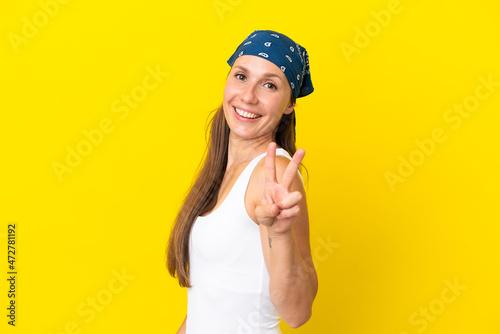 Young English woman isolated on yellow background smiling and showing victory sign