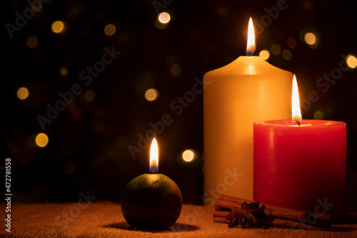 Burning Christmas candles with cinnamon and star anise on a dark background