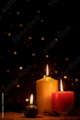 Burning Christmas candles with cinnamon and star anise on a dark background
