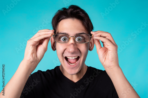 A funny man with glasses makes grimaces at the camera. Portrait of a guy against a blue background.