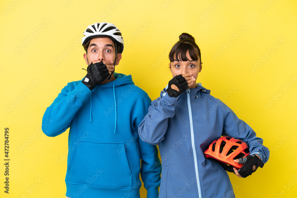 Obraz premium Young cyclist couple isolated on yellow background covering mouth with hands for saying something inappropriate