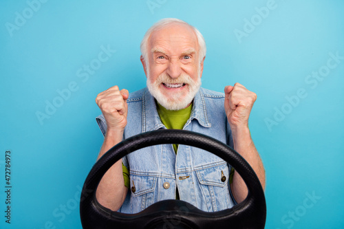 Photo of angry aggressive man pensioner dressed retro denim vest riding car showing fists isolated blue color background