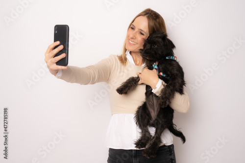 Young happy woman hugging her dog making a selfie with smartphone standing over white background.