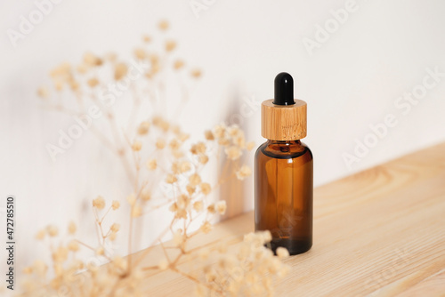 Amber dropper bottle with serum or essential oil on natural wooden background with daylight. Skincare products , natural cosmetic with with dry plants. Beauty concept for face body care