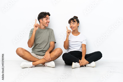 Young mixed race couple sitting on the floor isolated on white background unhappy and frustrated with something