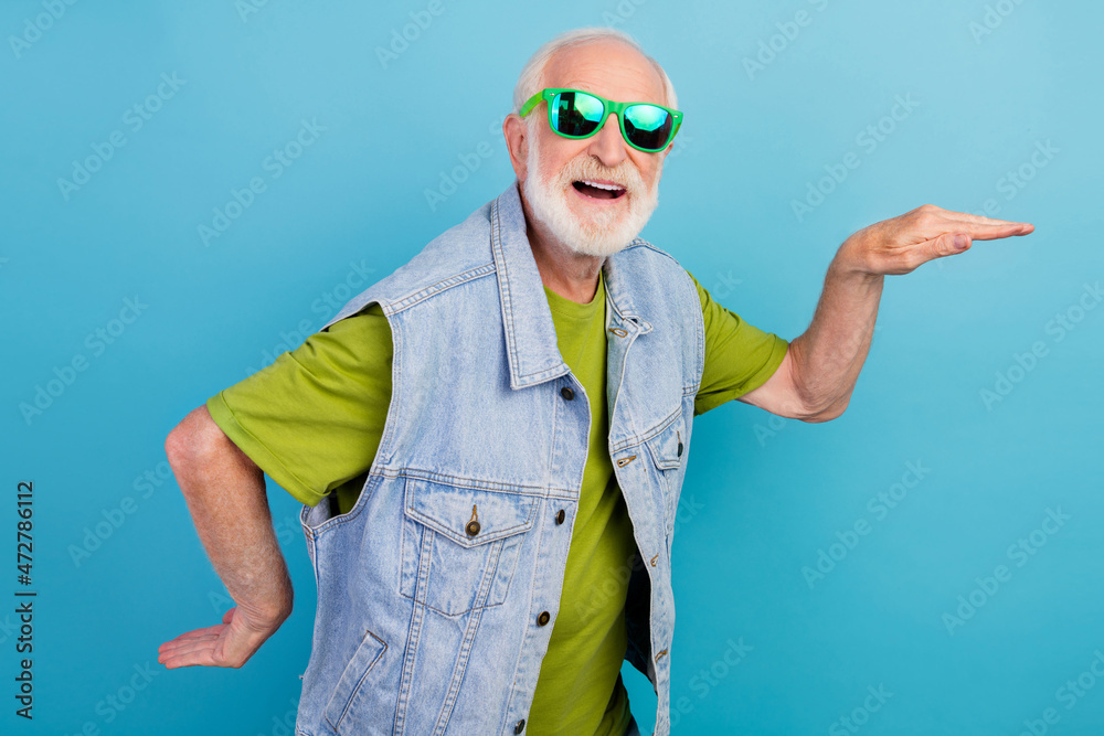 Photo of funky handsome man pensioner dressed retro denim vest dark eyewear smiling dancing isolated blue color background