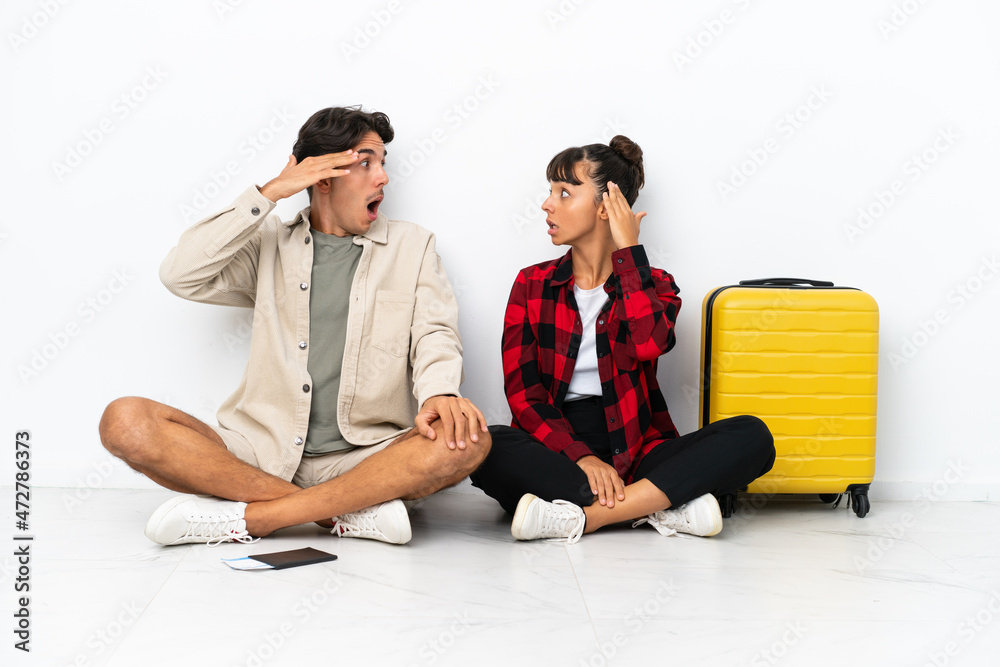 Young mixed race travelers couple sitting on the floor isolated on white background with surprise and shocked facial expression Young mixed race travelers couple sitting on the floor isolated on white background with surprise and shocked facial expression
