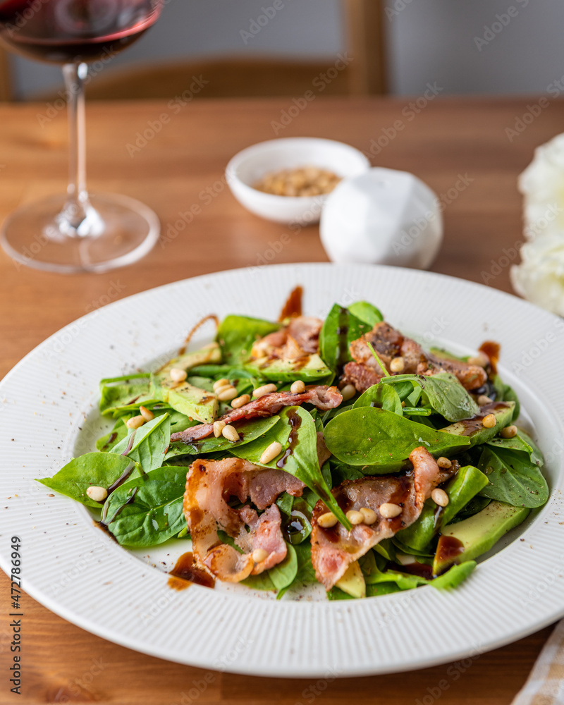 Salad with bacon, spinach, avocado and pine nuts in a white plate on the table Salad with bacon, spinach, avocado and pine nuts in a white plate on the table