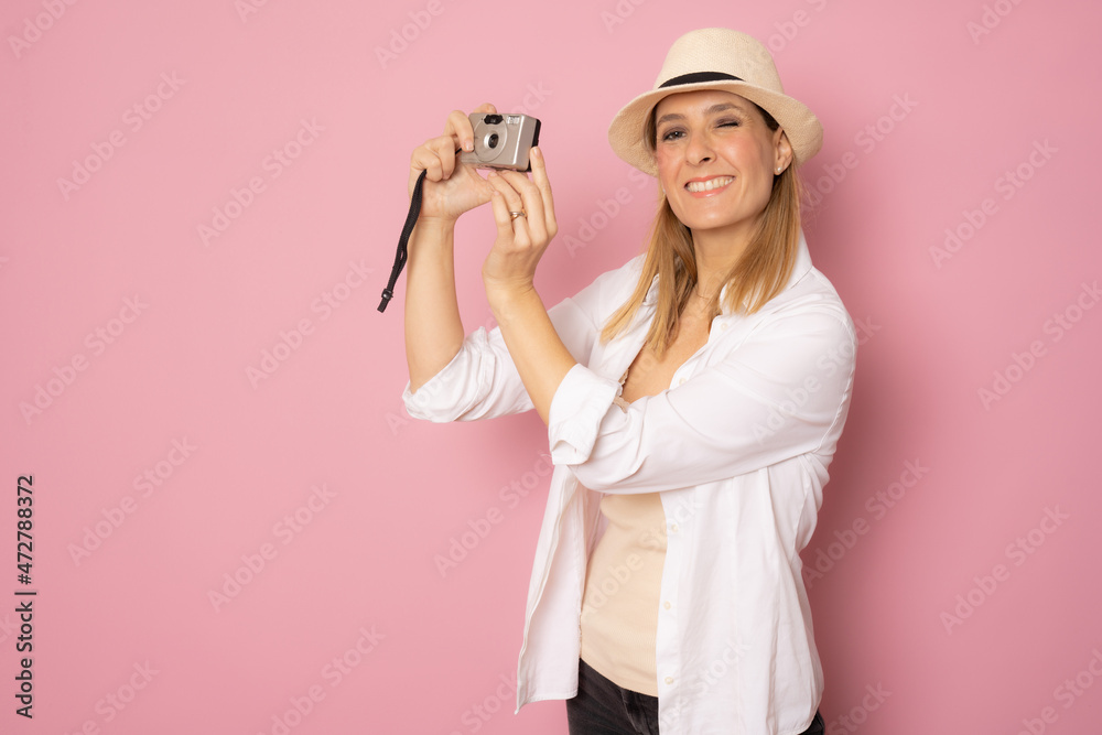 Happy smiling young woman wearing straw hat isolated over pink background with a camera in her hands Happy smiling young woman wearing straw hat isolated over pink background with a camera in her hands