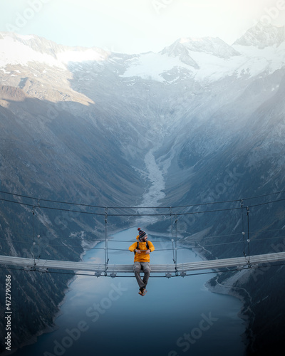 Canvastavla Man in yellow jacket sitting on a suspension bridge over a lake in Olpererhutte,