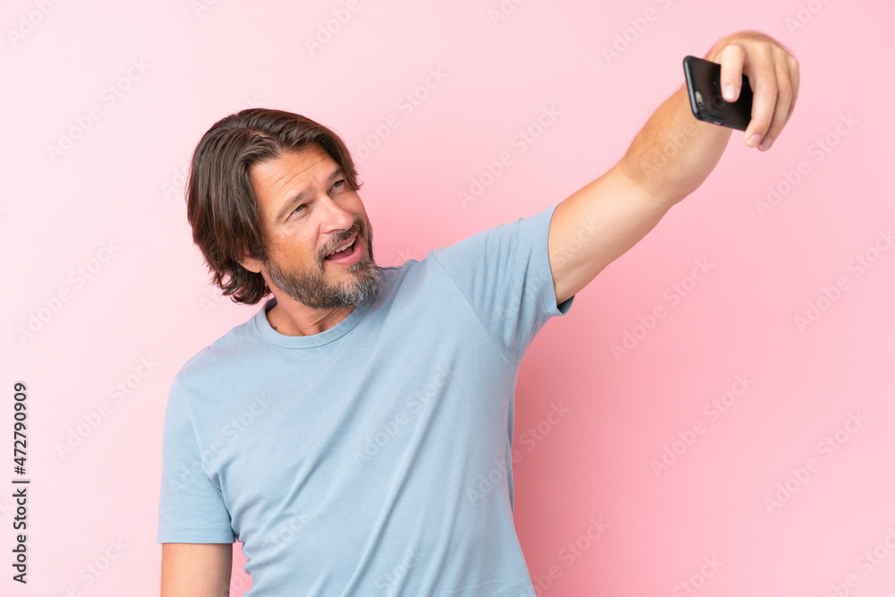 Senior dutch man isolated on pink background making a selfie with mobile phone Senior dutch man isolated on pink background making a selfie with mobile phone