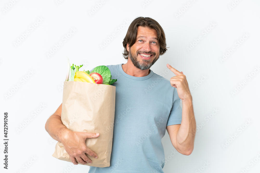 Senior dutch man holding grocery shopping bag over isolated background giving a thumbs up gesture Senior dutch man holding grocery shopping bag over isolated background giving a thumbs up gesture