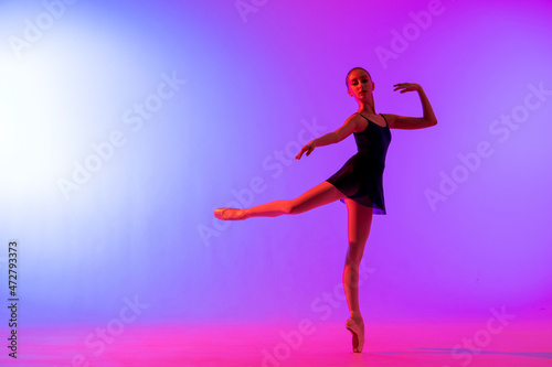 Beautiful young girl ballerina in pointe shoes and pink leotard silhouette on bright blue background.