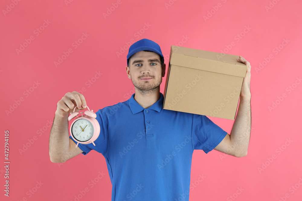 Delivery man holds box and alarm clock on pink background Delivery man holds box and alarm clock on pink background