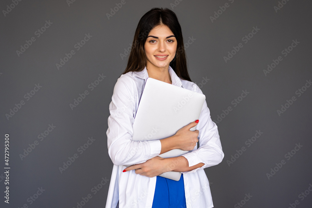 Young woman holding laptop and looking at camera over gray background Young woman holding laptop and looking at camera over gray background