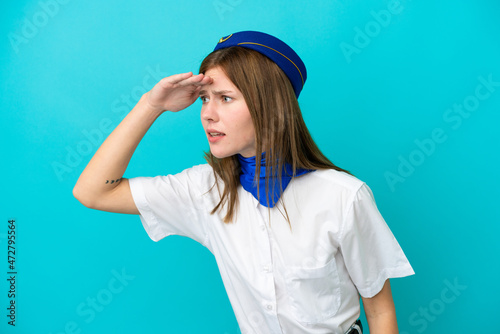 Airplane stewardess English woman isolated on blue background looking far away with hand to look something © luismolinero