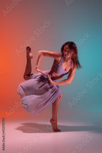 Portrait of young flexible contemp dancer dancing isolated on gradient blue orange background in neon. photo