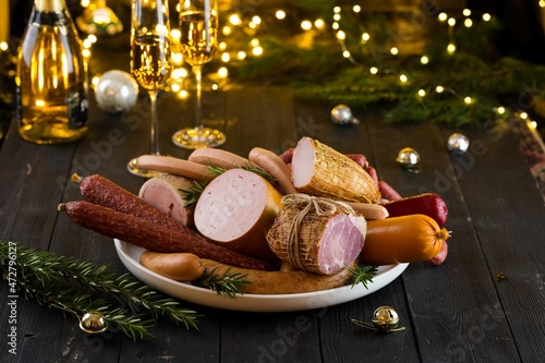 Fresh sausages and hams on new year or Christmas celebration table with champagne glasses and bokeh lights, delicious snack, spicy and high quality meat products made of pork and veal, beef.