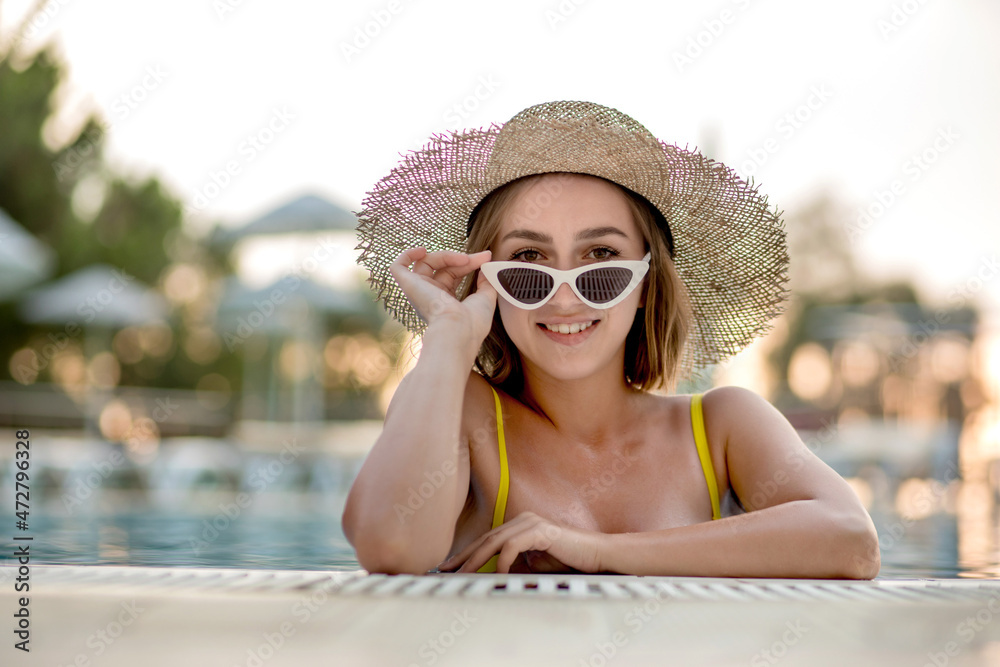 Beautiful woman in a hat and sunglasses relaxing in the pool