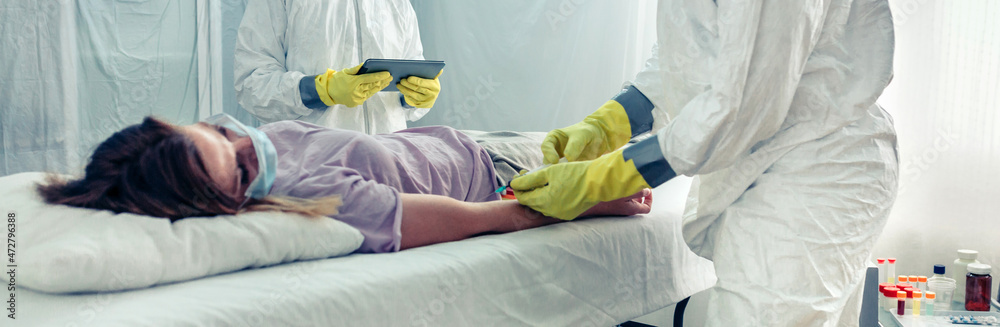 Obraz premium Doctors in bacteriological protection suit taking blood sample from patient lying on a gurney in a field hospital