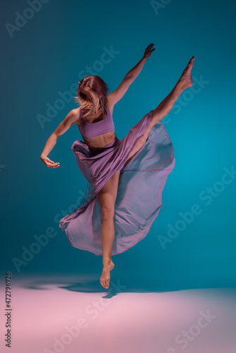 Young adorable flexible contemp dancer in lilac dress dancing isolated on gradient blue white background in neon.