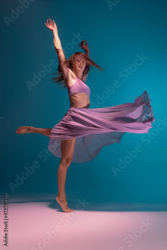 One young flexible contemp dancer in lilac dress dancing isolated on gradient blue white background in neon.