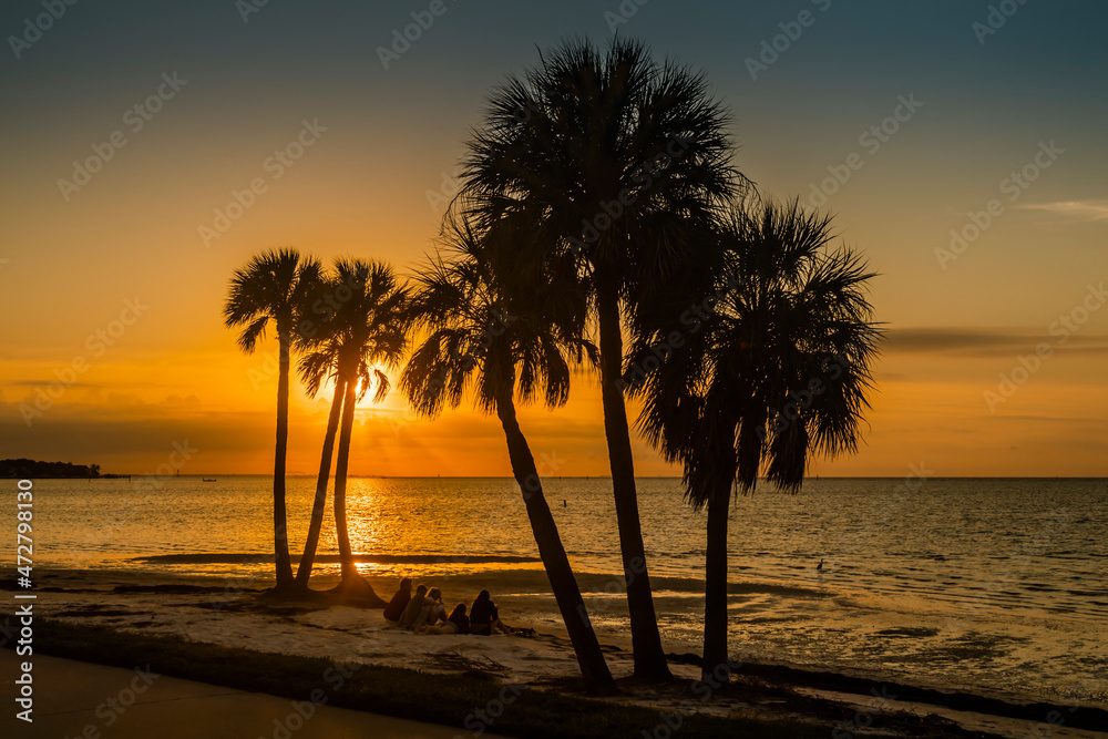 People sitting on the beach watching the sunrise over Old Tampa Bay