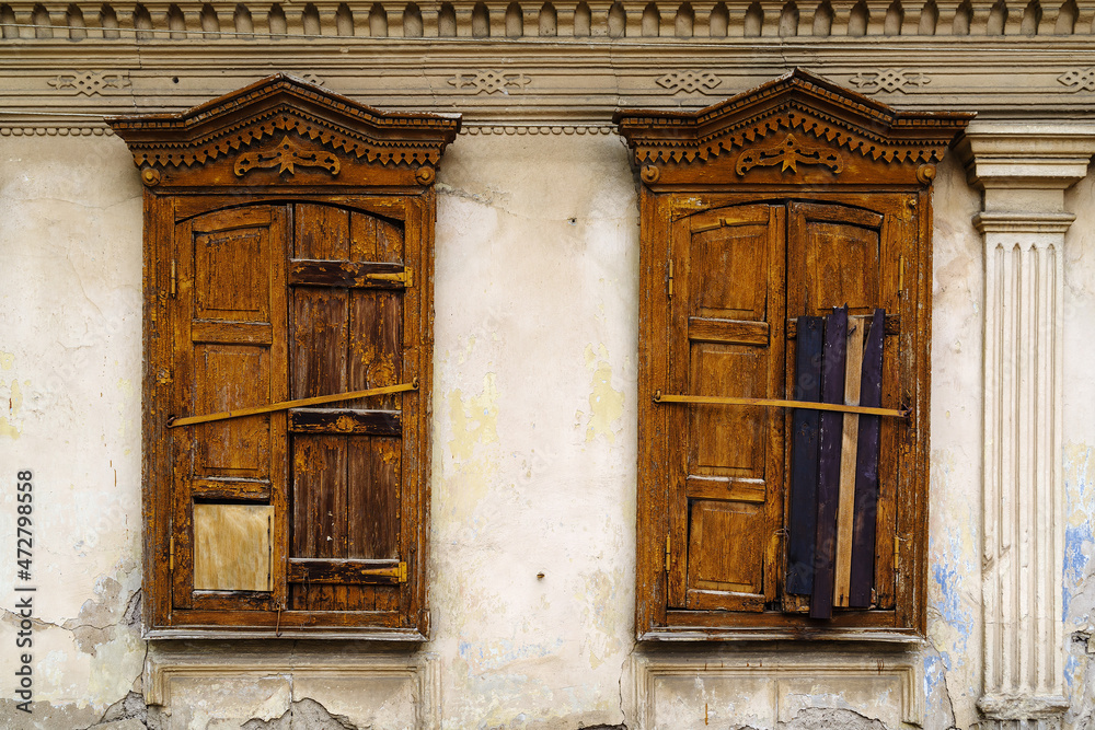 Carved windows with closed wooden shutters on the facade of a dilapidated old building. The picture was taken in Russia, in the city of Orenburg