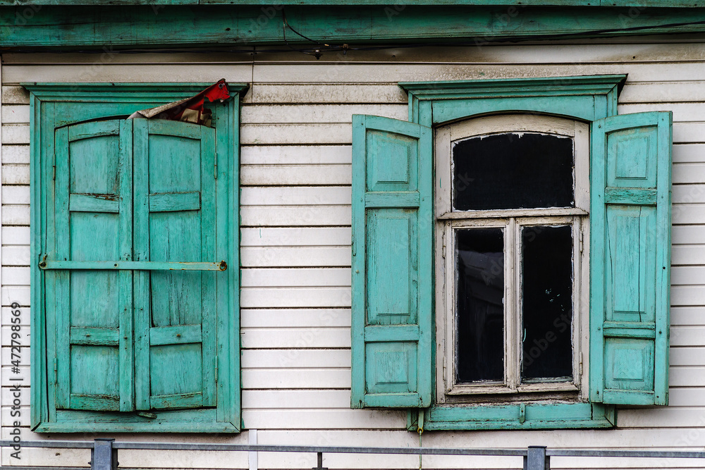 An old wooden house with green shutters and platbands, sheathed with modern siding. The picture was taken in Russia, in the city of Orenburg