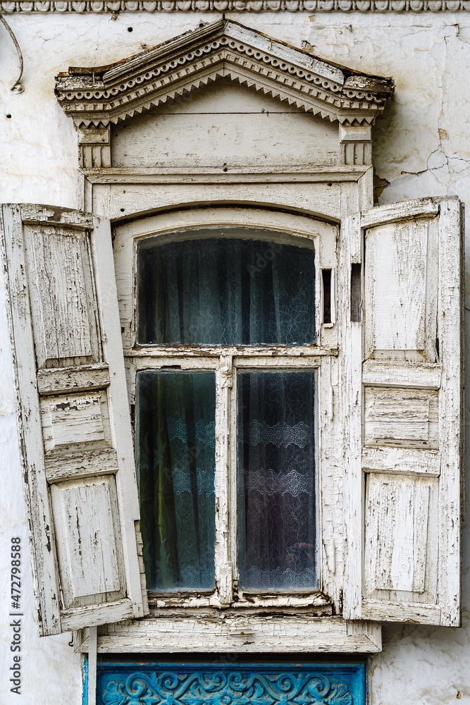 A window with wooden shutters and carved frames of the old house, with stucco elements on the facade. The picture was taken in Russia, in the city of Orenburg