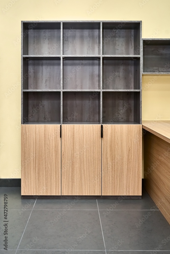 Office storage cabinet for documents with empty shelves made of laminated chipboard with wood and stone texture pattern in spacious office Office storage cabinet for documents with empty shelves made of laminated chipboard with wood and stone texture pattern in spacious office