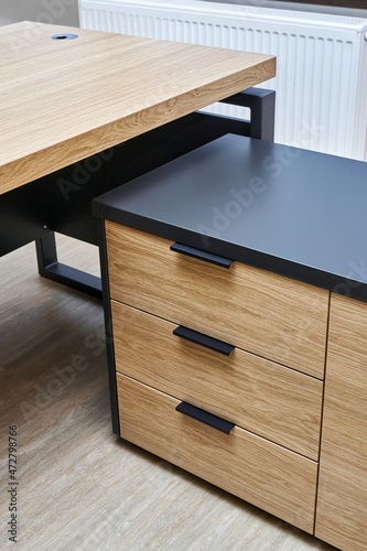 Large executive desk made of oak timber veneer with dark grey enamel in trendy minimal style stands in light spacious office closeup view