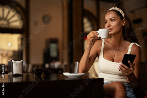 Stylish young woman drinking coffee at cafe. Beautiful girl enjoy in fresh coffee.