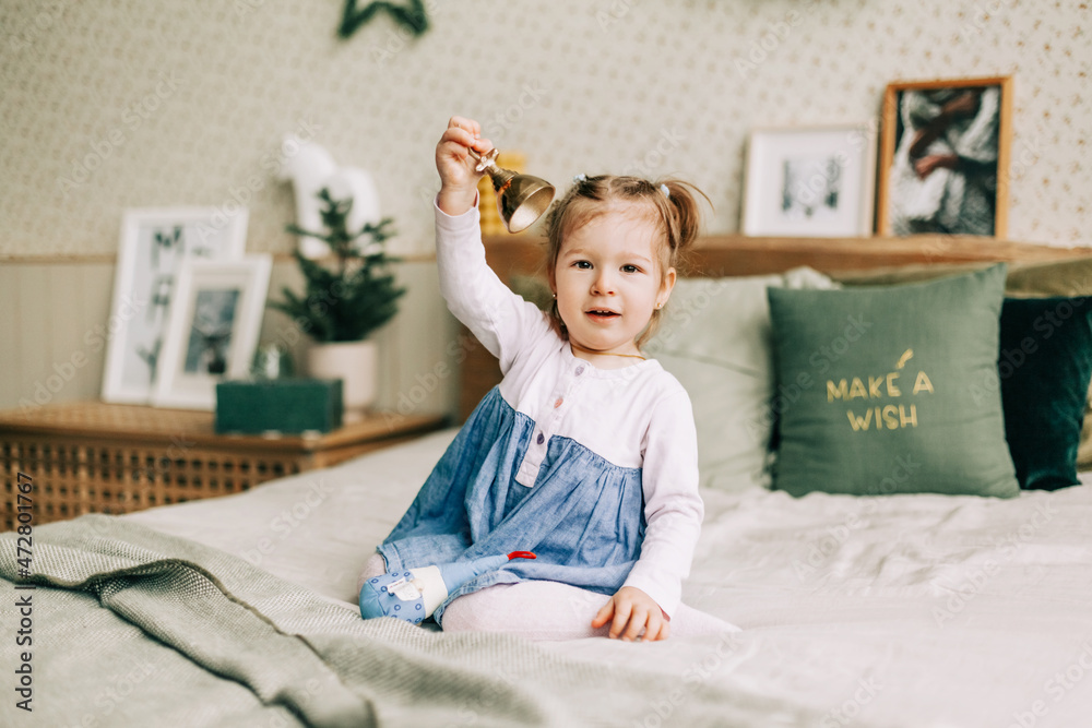 Naklejka premium A happy girl is playing on the bed on Christmas morning in a room decorated for Christmas or New Year. Childhood, festive morning, Christmas mood