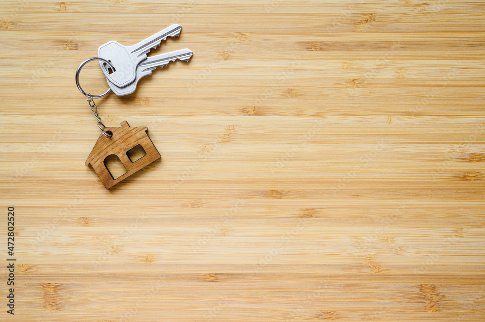 Keys to a new house with a house-shaped keyring on a wooden background. Keys to a new house with a house-shaped keyring on a wooden background.