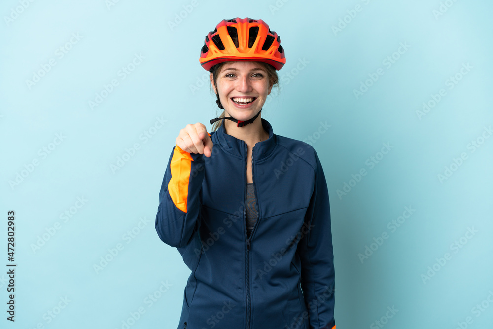 Young cyclist woman isolated on blue background surprised and pointing front - obrazy, fototapety, plakaty 