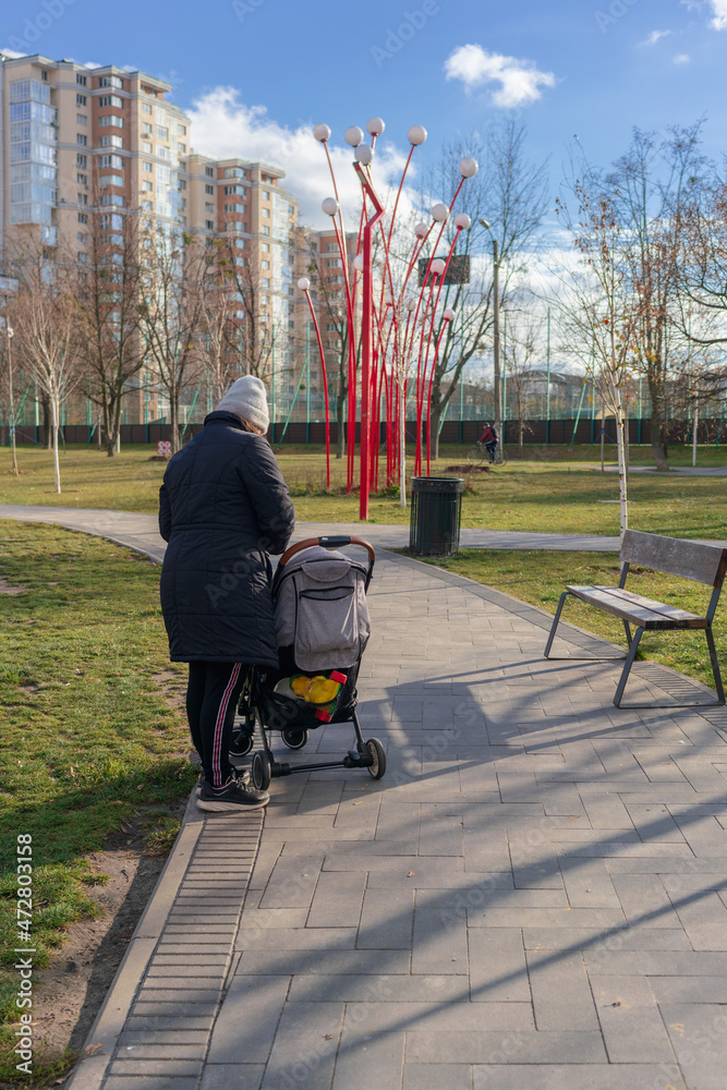 Obraz premium Mom with a baby carriage in an autumn day in a city park on a cobbled stone tiled walkway