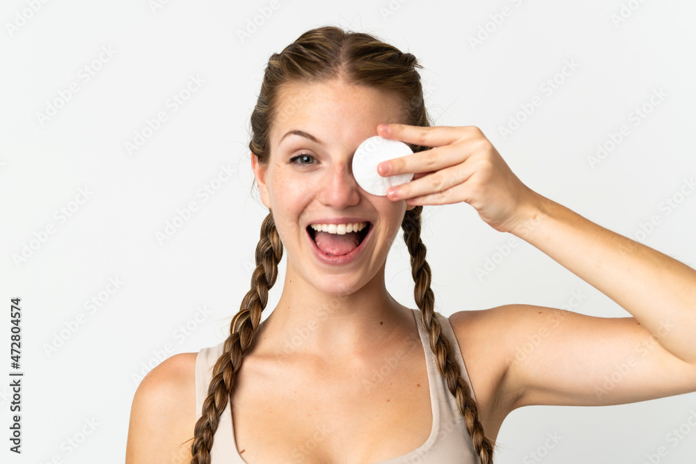 Obraz premium Young caucasian woman isolated on white background with cotton pad for removing makeup from her face and smiling