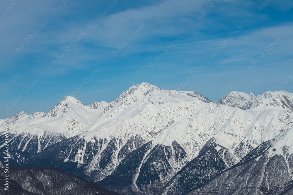 Snowy mountain ranges against a background of blue sky with clouds. Snowy mountains. A beautiful winter landscape.